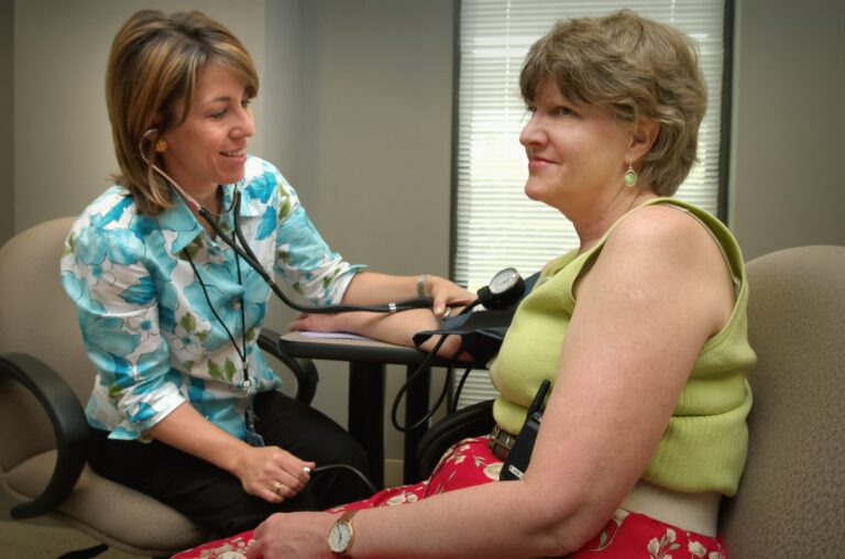 a woman with a stethoscope taking blood pressure of a woman in a chair