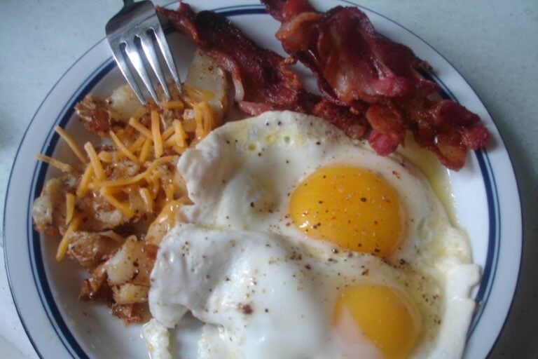 High-cholesterol eggs sunny side up, bacon, and home fries with cheddar cheese