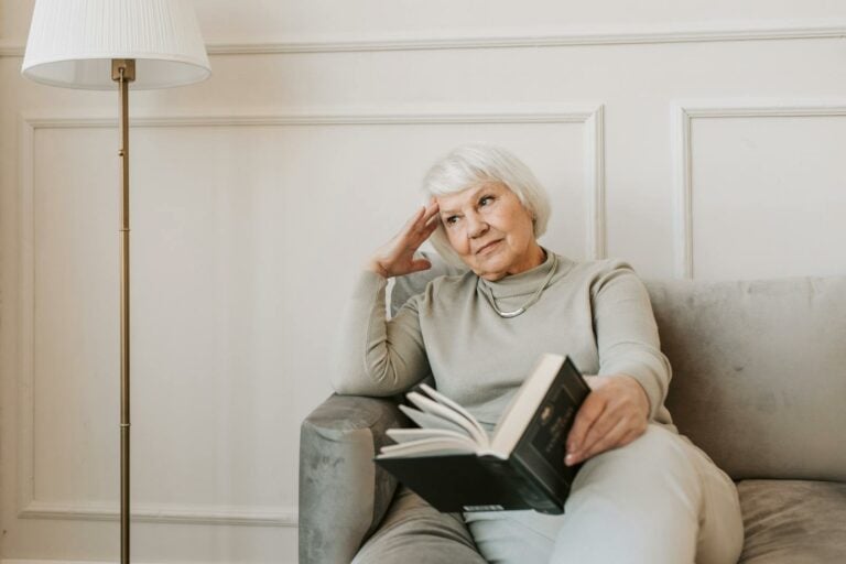 Pensive Alzheimer's Caregiver Sitting on Gray Couch with a Book
