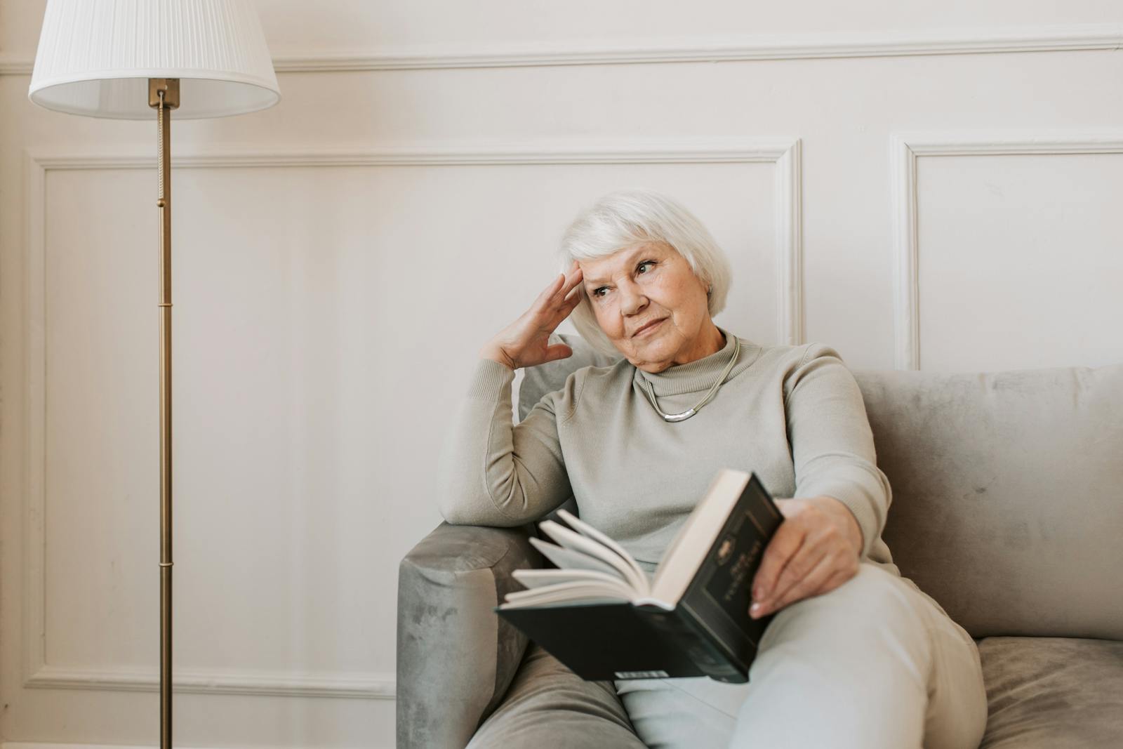 Pensive Alzheimer's Caregiver Sitting on Gray Couch with a Book
