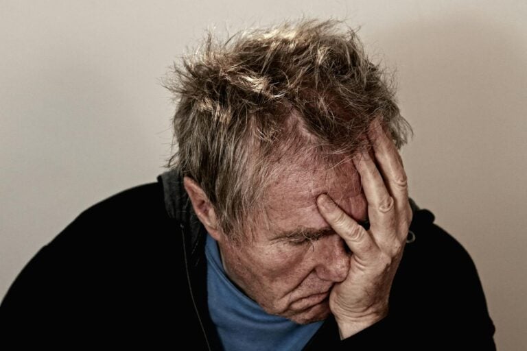 Portrait of an elderly man feeling stress and disappointment, holding his head in his hands.