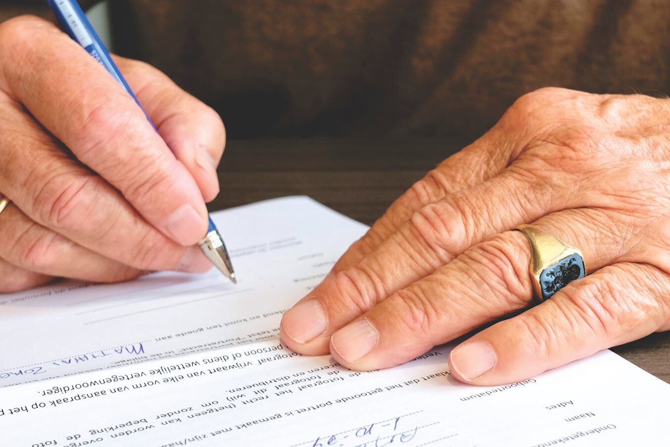 Close-up of a senior adult signing a legal document with a focus on hand and gold ring.