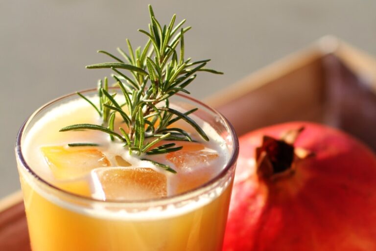 Rosemary rising out of clear drinking glass with yellow liquid inside