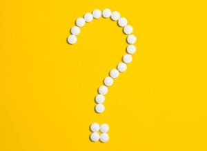 White pills arranged in a question mark shape on a bright yellow background, symbolizing medical queries.